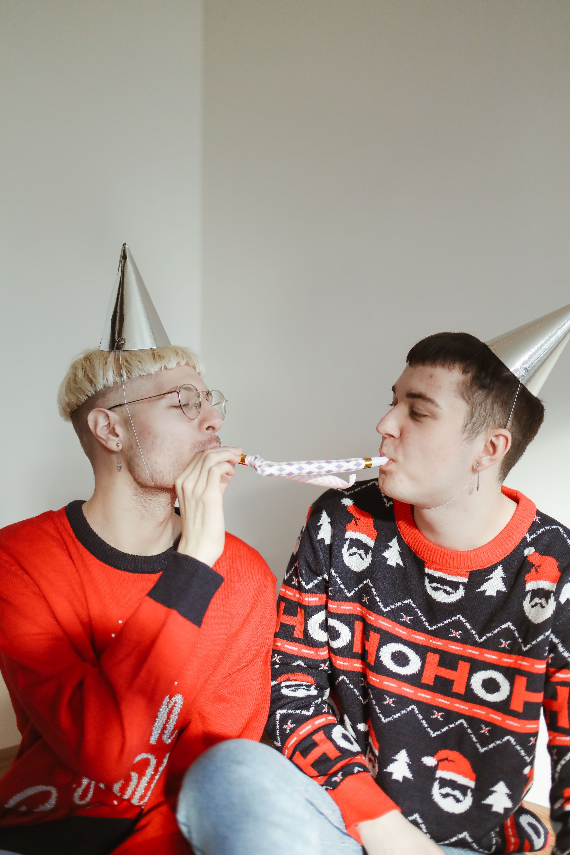 两个穿着节日毛衣、戴着派对帽子的男人正在室内进行欢乐的庆祝活动