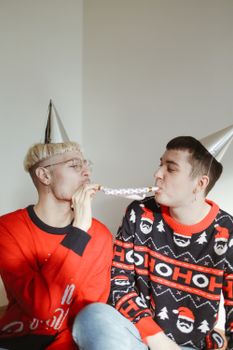 两个穿着节日毛衣、戴着派对帽子的男人正在室内进行欢乐的庆祝活动