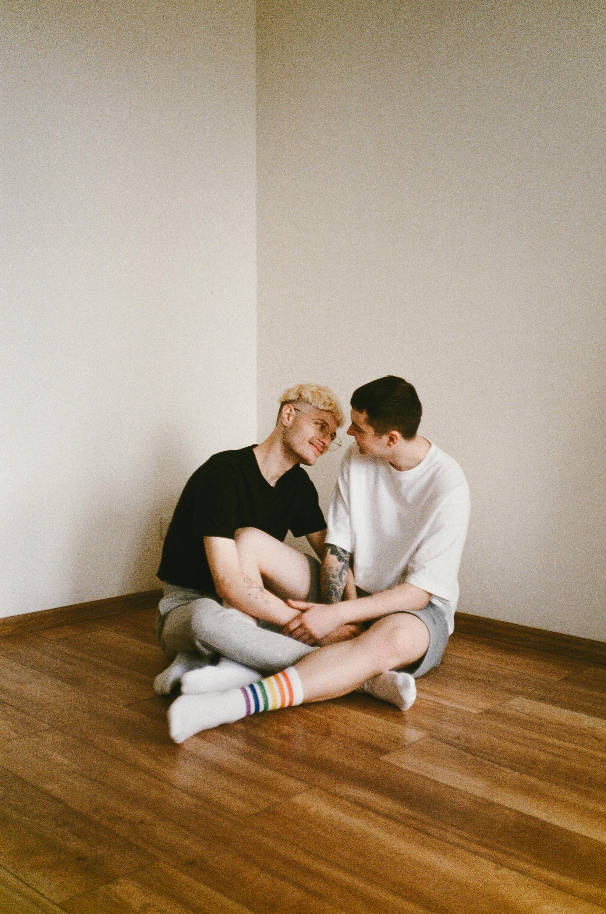 A happy couple sitting closely on a wooden floor, sharing a tender moment indoors.