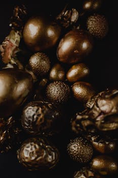 Artistic still life of gold-painted fruits and nuts on a black background.