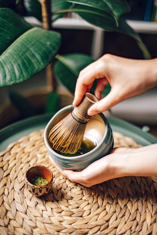 Person Holding Bamboo Whisk and Ceramic Bowl with Liquid 