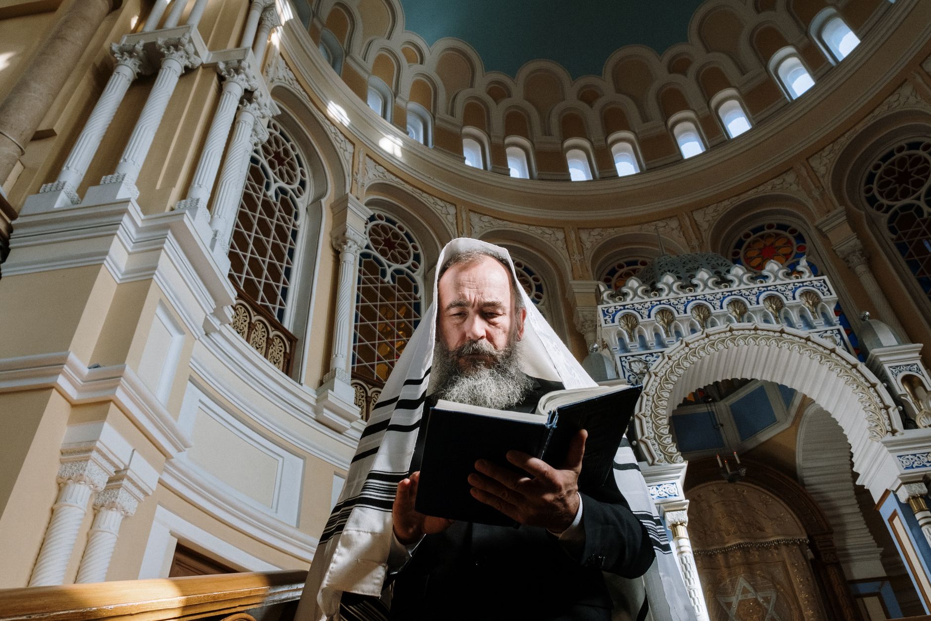 A rabbi in traditional Jewish attire reads the Torah inside a beautifully ornate synagogue.