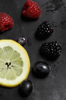 A close-up of assorted fresh berries and a lemon slice on a dark background, showcasing healthy fruits.