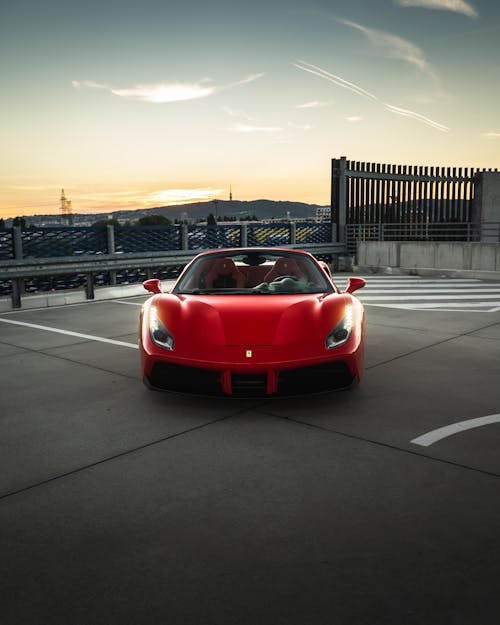 Modern prestige red automobile with bright luminous headlights under cloudy sky in bright sunset