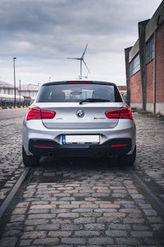 Rear view of a silver car parked on cobblestone in Antwerp, showcasing an urban industrial backdrop.