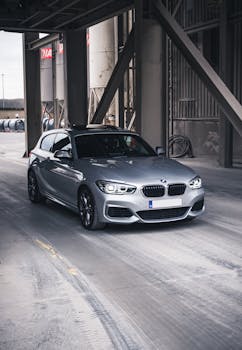 A shiny silver luxury car parked under an industrial structure in Antwerp, Belgium.