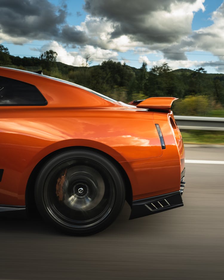 Bright Orange Car Driving Fast On Asphalt Road