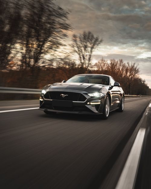 Free New expensive automobile driving fast on asphalt road neat leafless trees under cloudy sky Stock Photo