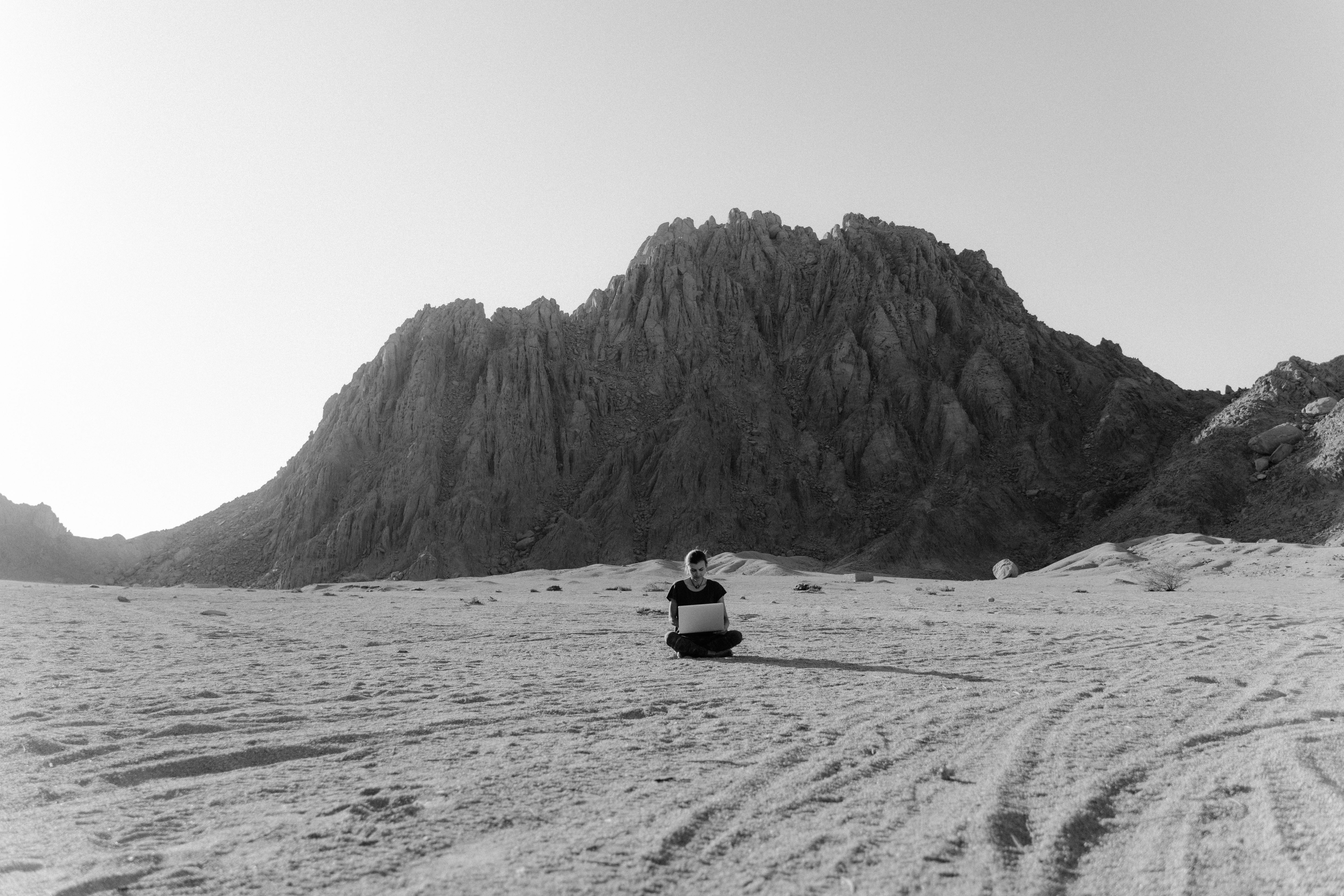 person sitting on sand near mountain