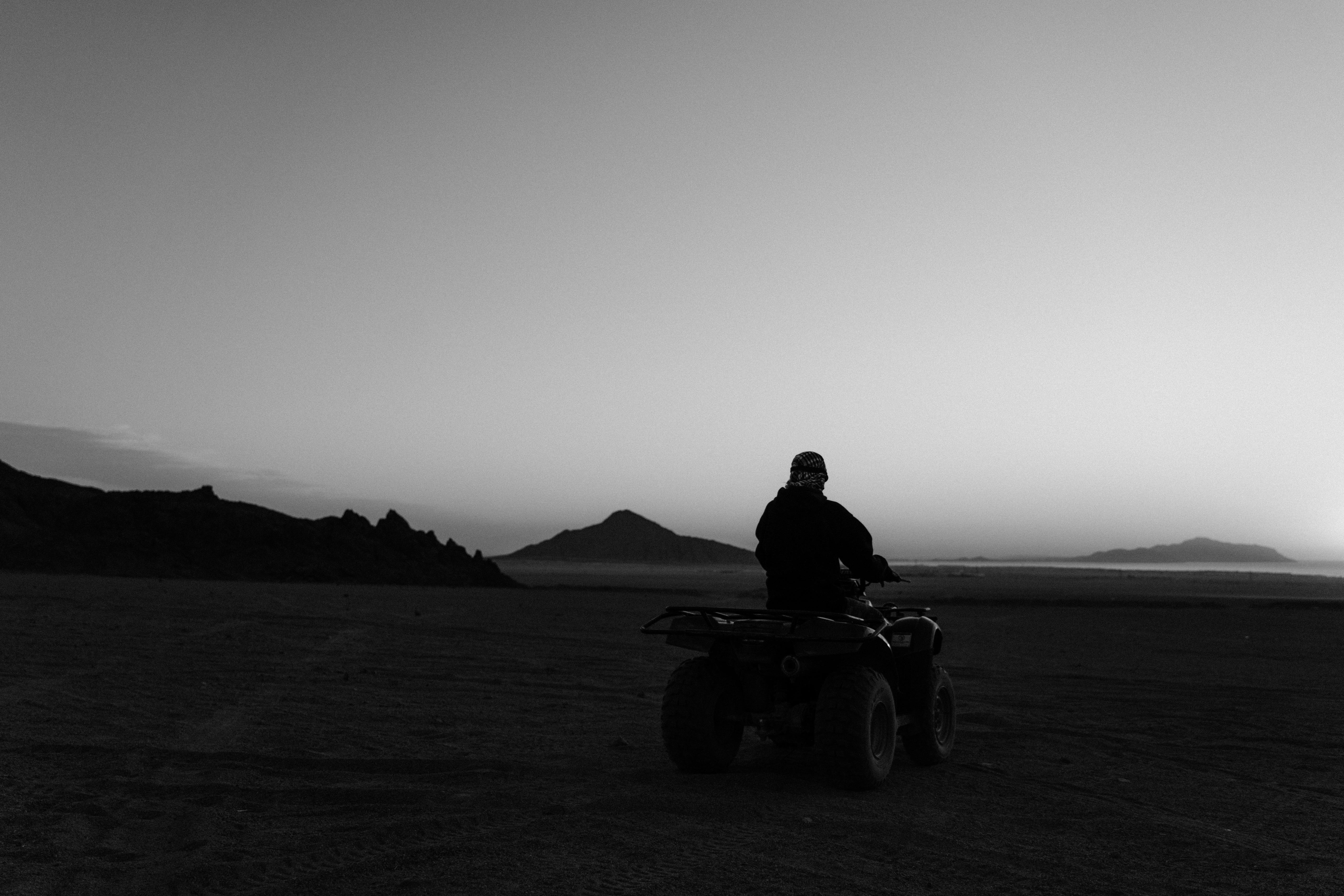A lone rider on an ATV explores a vast desert landscape at twilight in monochrome.