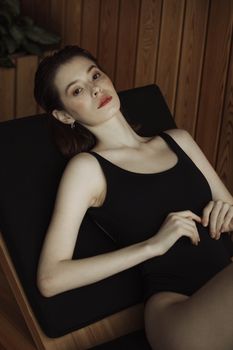 一名穿着黑色泳衣的女子靠在室内木墙边的椅子上