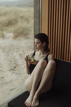 一名年轻女子穿着泳衣，坐在海滩边的室内喝茶
