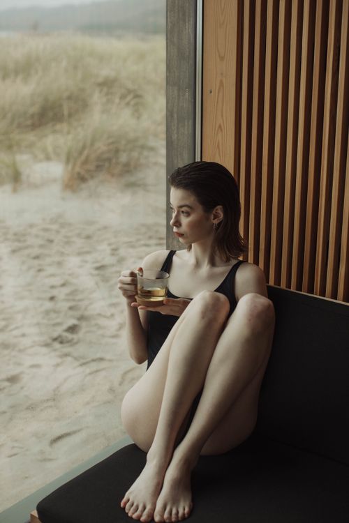 Free A young woman in a swimsuit sitting indoors by the beach, enjoying a cup of tea. Stock Photo