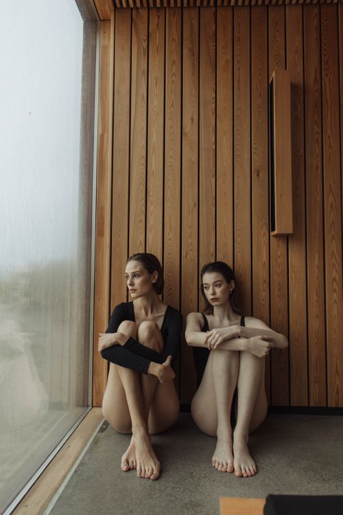 Free Two women sitting in a modern, wooden interior by a large window, exuding calmness and relaxation. Stock Photo