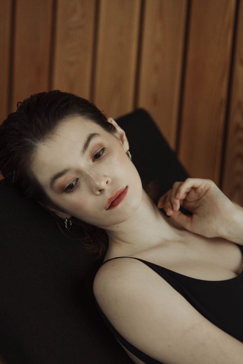Free A serene portrait of a woman with a brunette hairstyle, wearing earrings and a black tank top, posing against a wooden backdrop. Stock Photo