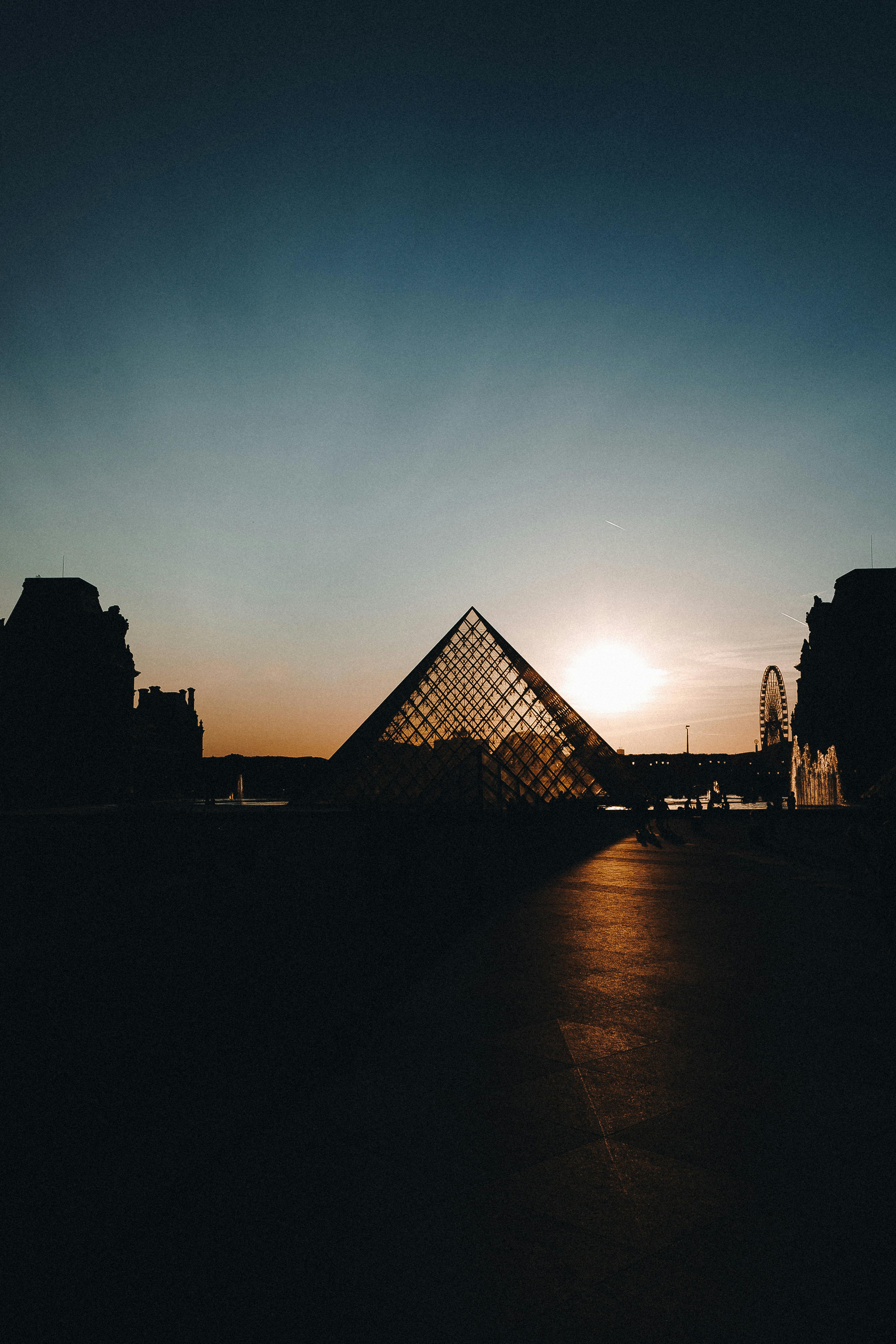 A stunning silhouette of the Louvre Pyramid against a sunset sky in Paris, France.