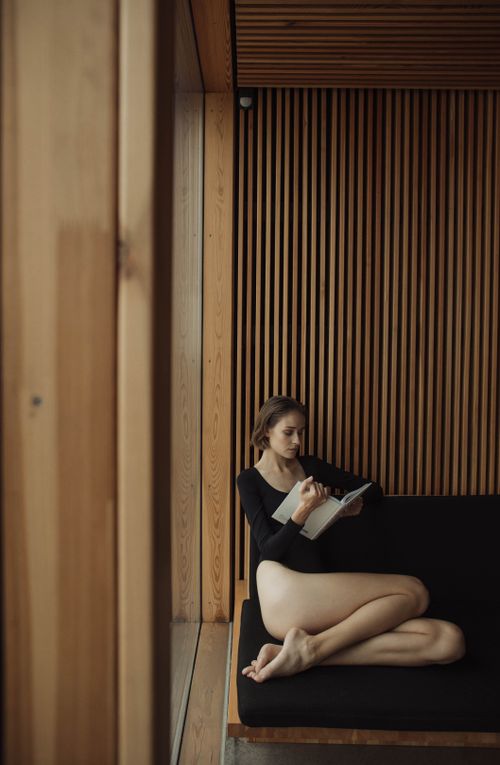 Free A woman in a black outfit reading a book on a cozy wooden couch, indoors. Stock Photo