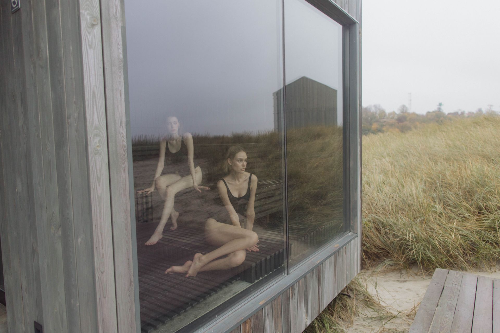 Woman sitting in a sauna with a reflective glass panel showcasing an outdoor landscape.