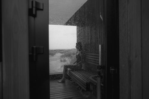 Free A woman sits in a sauna gazing out at a tranquil landscape through a glass door. Stock Photo