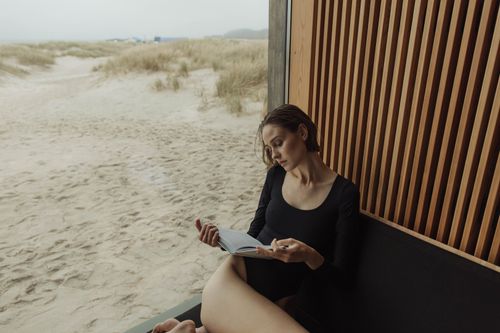 Free Woman enjoying a relaxing moment reading a book by a beachside window. Stock Photo
