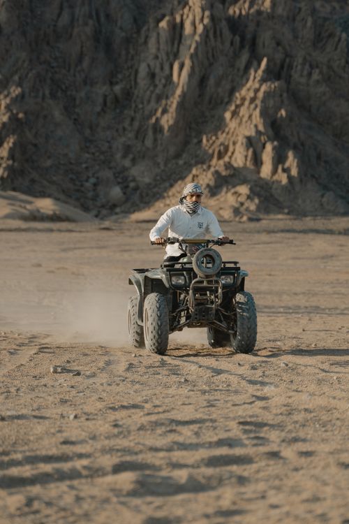 Free A person on an ATV riding through rocky desert landscape, creating dust clouds. Stock Photo