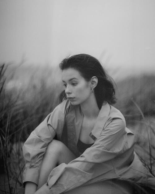 Grayscale Photo of Woman in Jacket Sitting on Grass