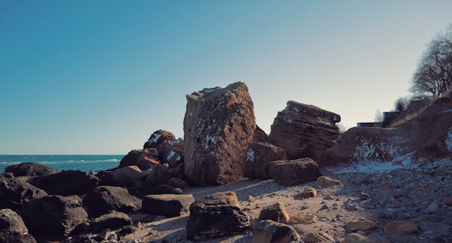 Idyllic seascape featuring large boulders on a serene, rocky shore under a cloudless sky.