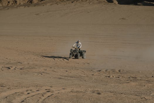 A person navigating an ATV through a vast, sandy desert landscape.