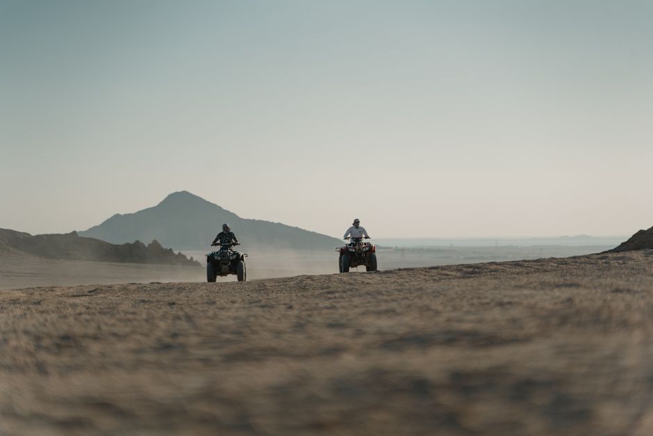 Two people riding ATVs across a vast and scenic desert landscape.