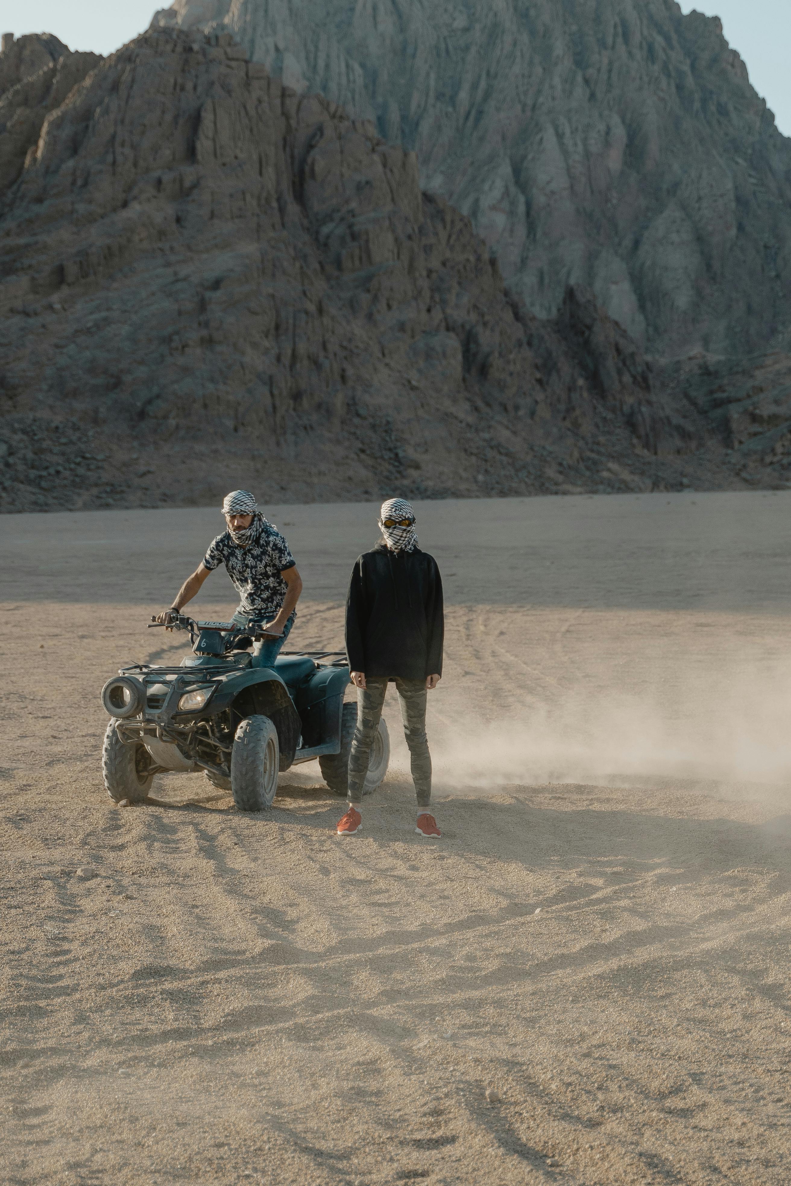 Two people enjoying a thrilling ATV ride across a vast desert terrain, creating dust trails.