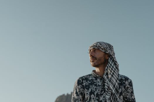 一名男子身穿图案衬衫、头戴头巾，站在晴朗的天空下