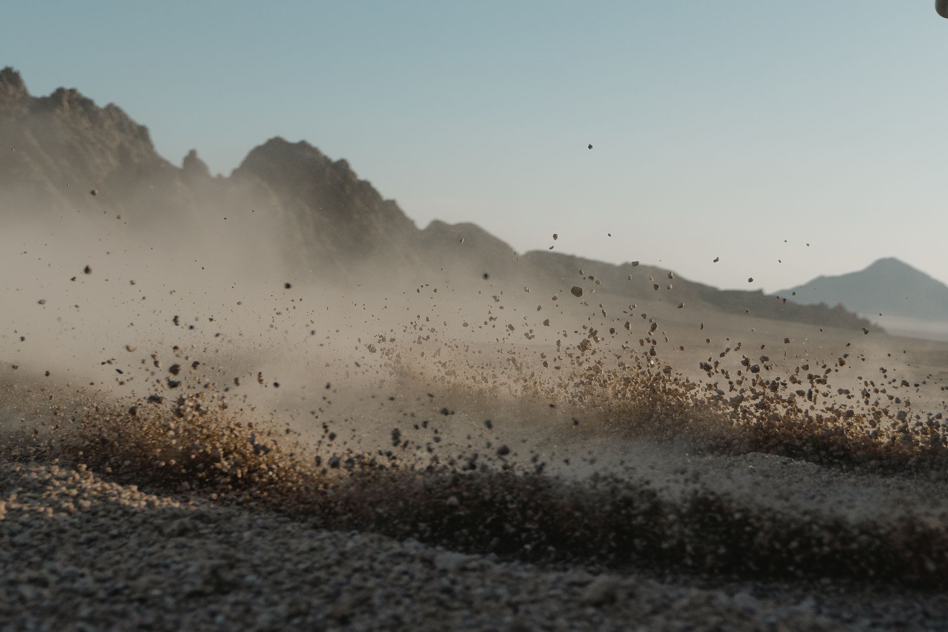 Close-up of dust cloud forming in rocky desert landscape with mountain backdrop.