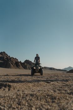一名男子驾驶全地形车，穿过广阔的沙漠，背景是岩石山脉