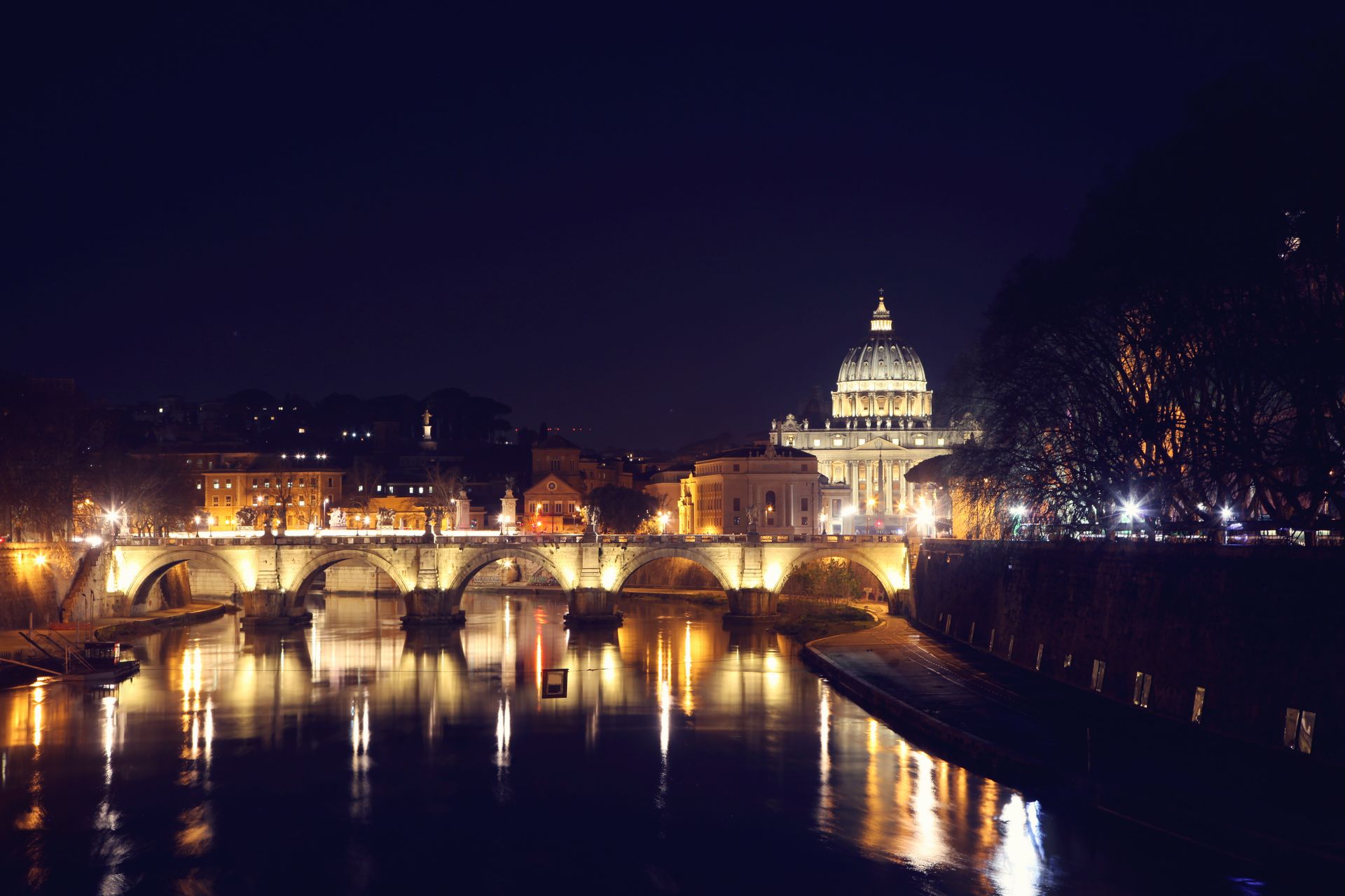 Picturesque night cityscape with dome of famous St Peters Basilica dominating skyline of Rome with illuminate arched bridge over Tiber river