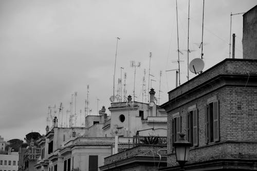 Black and white of aged residential houses with modern antennas on roofs against overcast sky in Rome