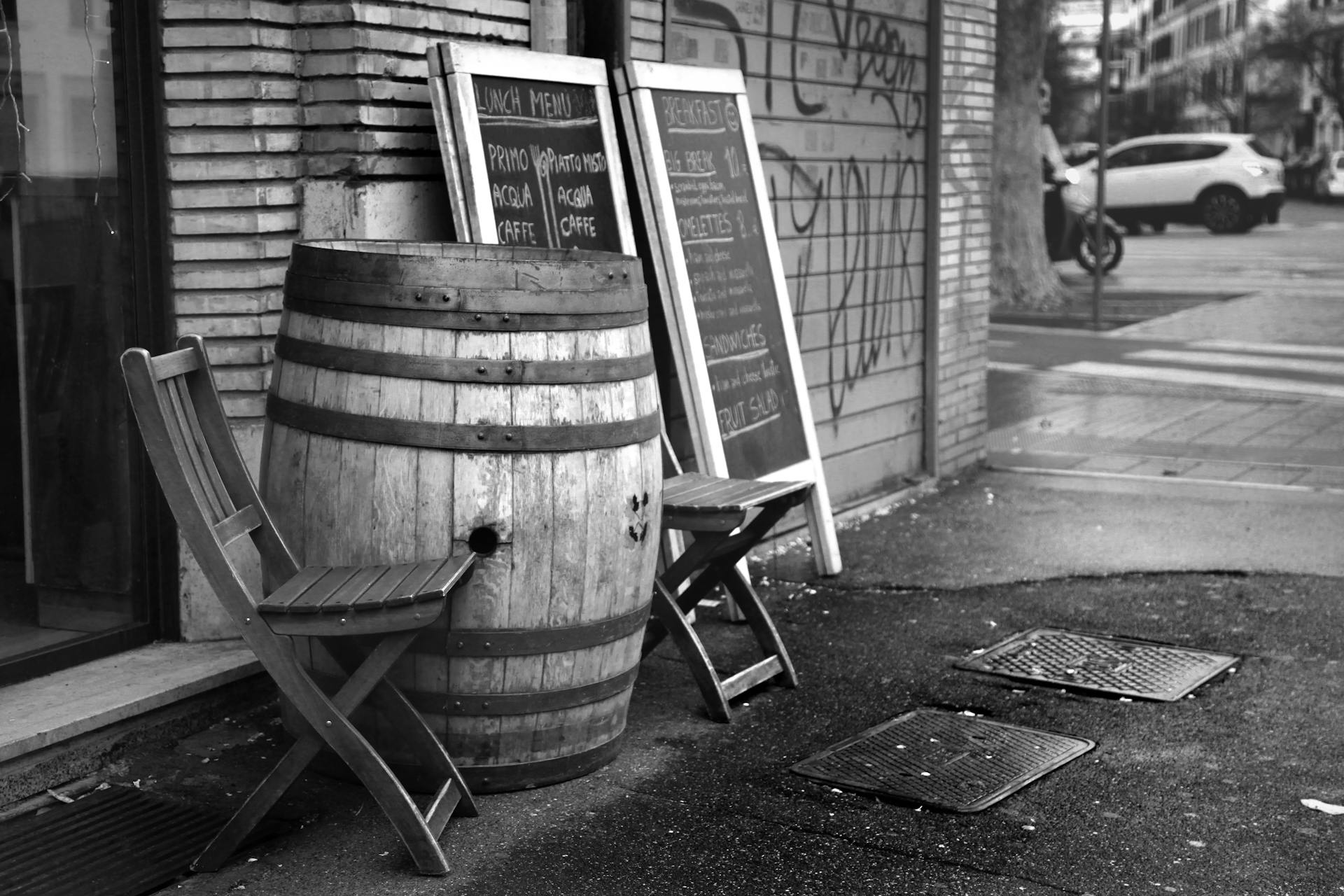 Black and white wooden barrel and chairs placed outside coffee shop near menu chalkboard