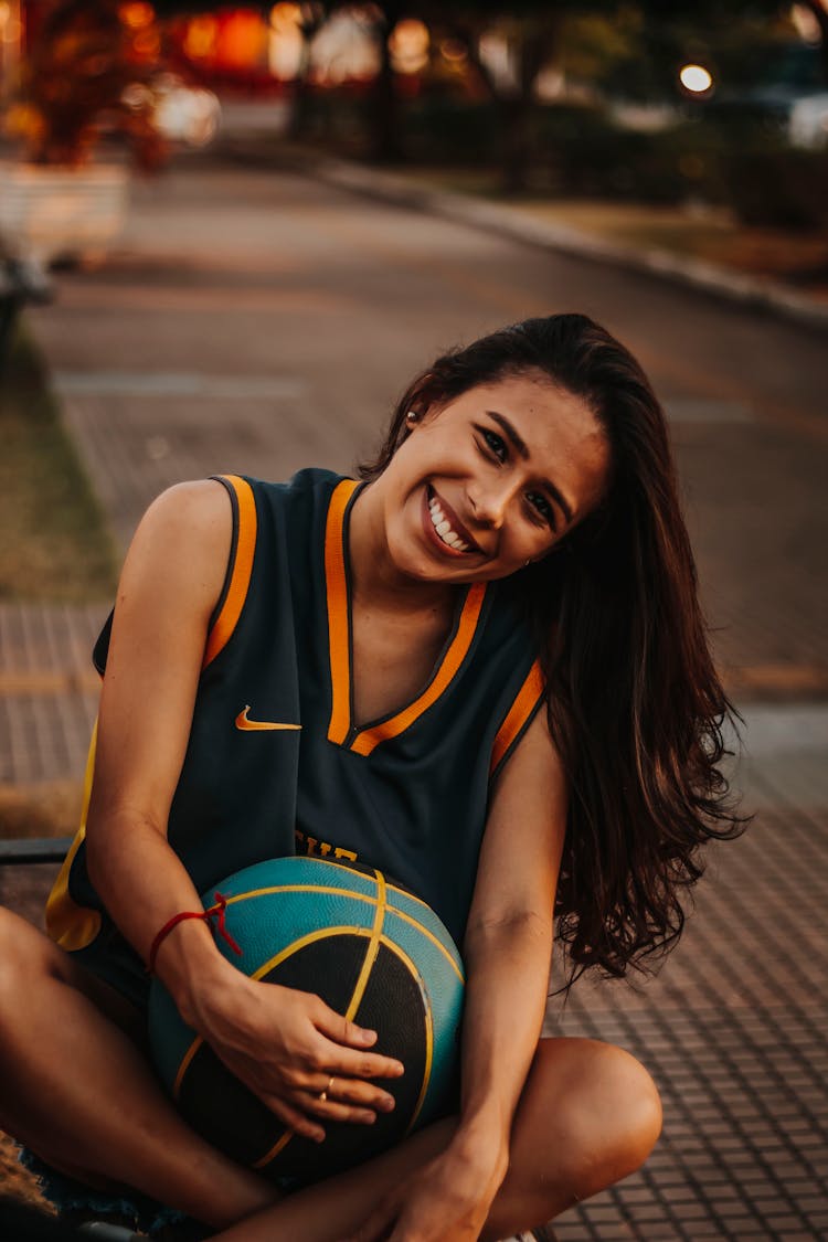 Cheerful Female Basketball Player Sitting On Ground With Ball