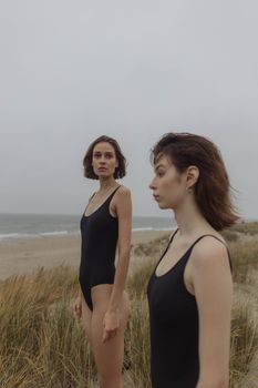 天空阴沉的沙滩上站着两名身穿黑色泳衣的女子