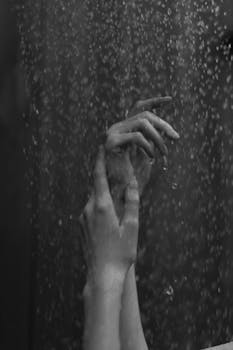 Artistic grayscale close-up of hands with water droplets for a moody atmosphere.