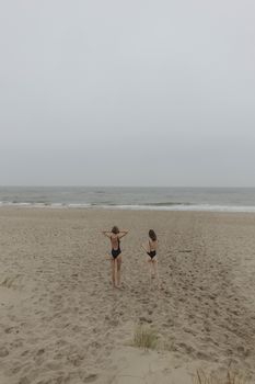 两名穿着泳衣的成年人沿着多云海景的沙滩散步