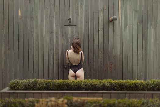 一名女子穿着黑色泳衣，靠在木墙上淋浴