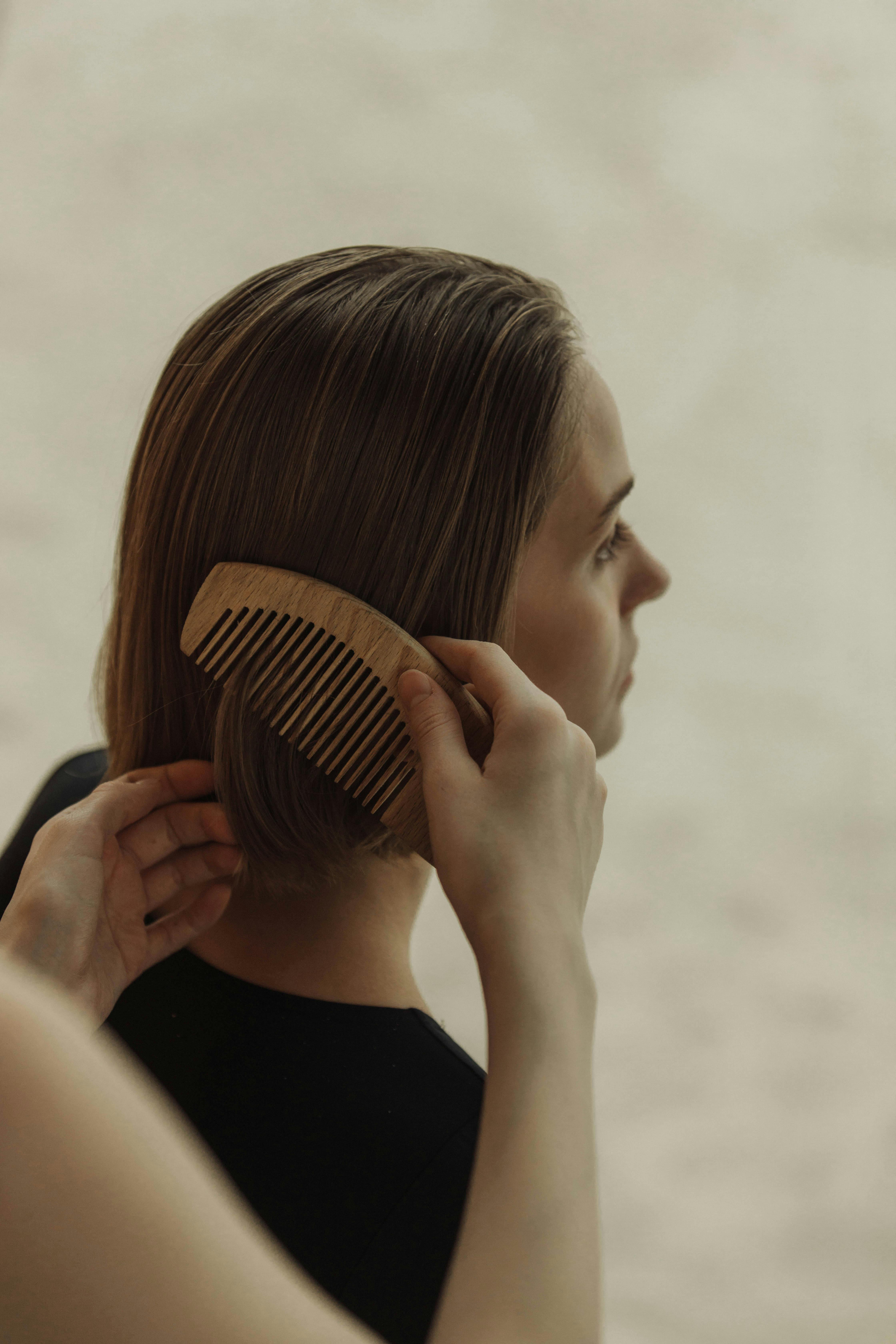 Close-up of a woman combing short hair with a wooden comb, indoors.