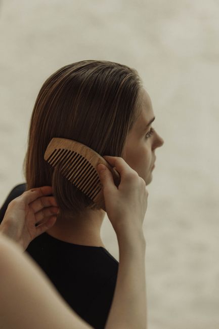 Fotomural Primer plano de una mujer peinando su cabello corto con un peine de madera, en interiores.