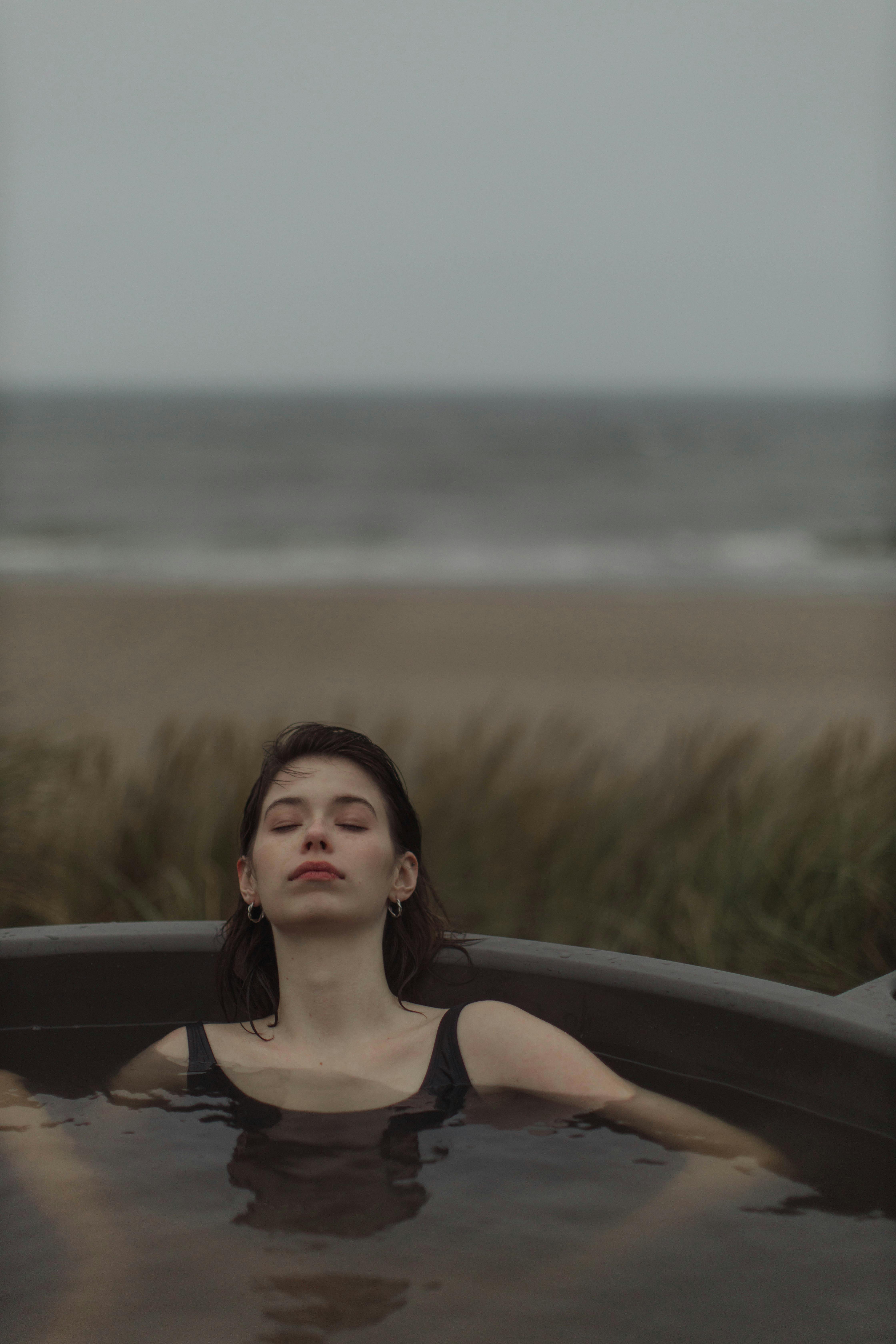 一个女人闭着眼睛，在宁静的海滩背景下的室外按摩浴缸中放松