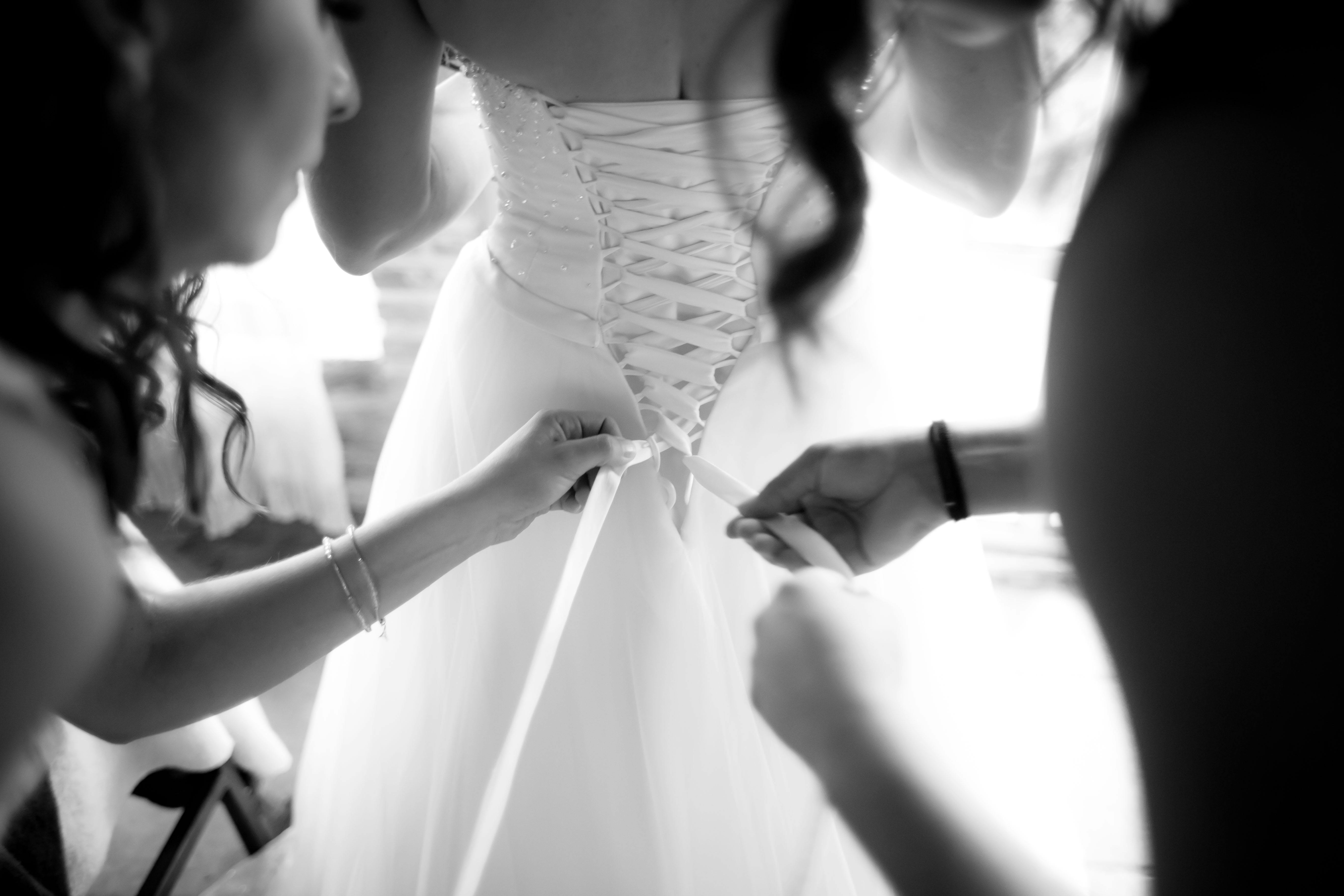 A bride getting ready as her wedding gown is tied by bridesmaids in black and white.