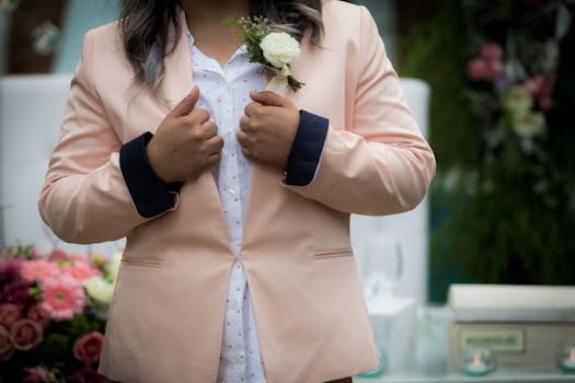 A person wearing a peach blazer with a white floral boutonniere, elegant and stylish.