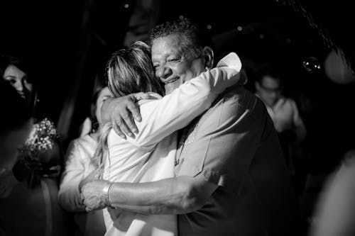 Black and White Photo of a Man and Woman Hugging among the Crowd at a Reception 