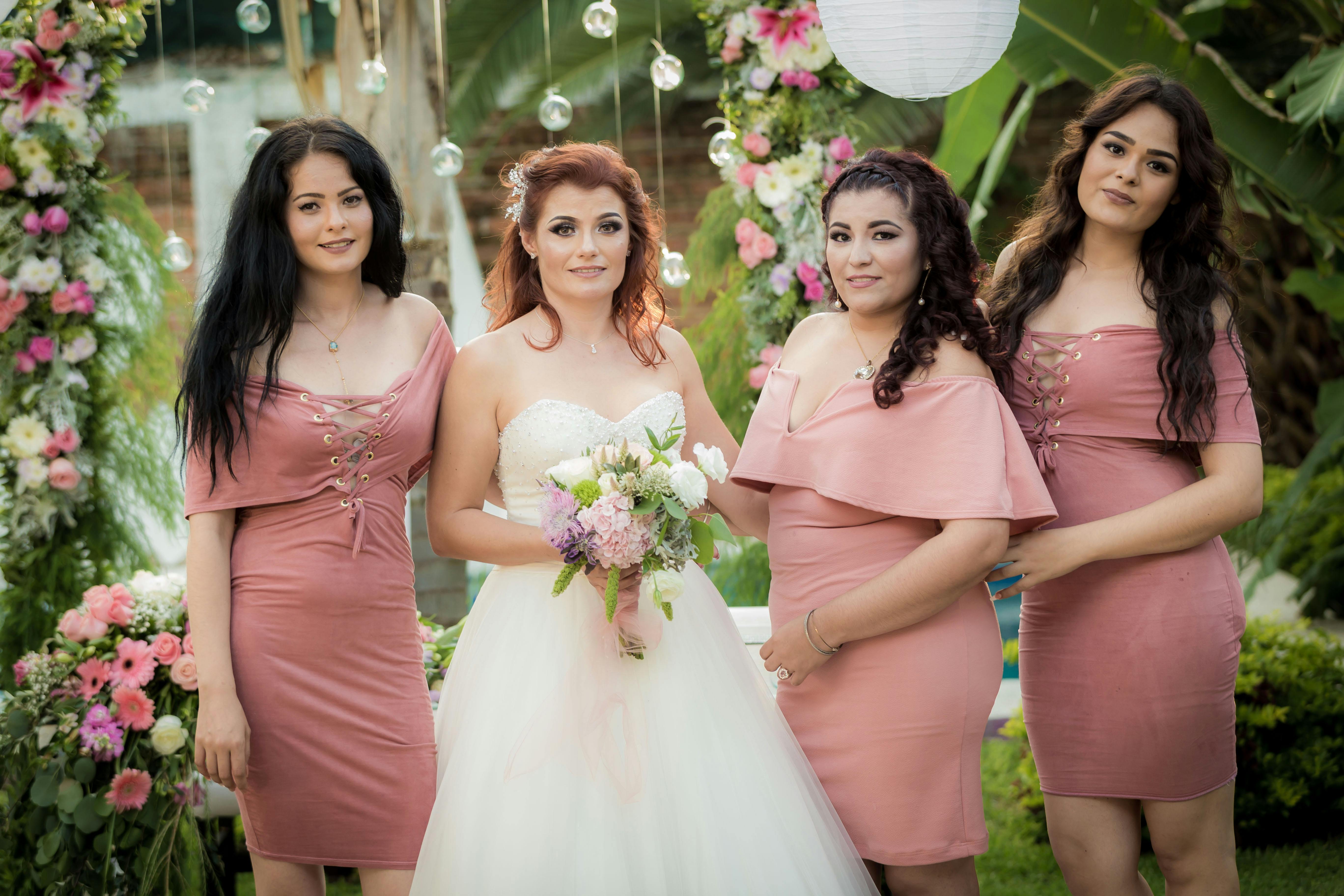 Bride and bridesmaids in pink dresses posing in a lush garden setting with floral decorations.