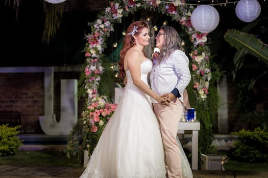 Beautiful same-sex couple exchanging vows under floral arch at night wedding.