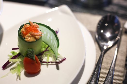 A delicate sushi appetizer featuring cucumber, salmon roe, and garnished with cherry tomato on a white plate.